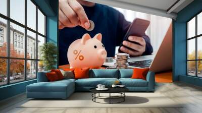 Interest rates, saving account, profit, financial, Investment loans concept. Percentage icon on pink piggy bank while man holding coin to put on it while using online banking app on mobile smartphone. Wall mural