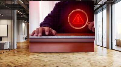 Virus alert. Red triangle icon, System hacked error sign, malware, attention danger symbol warning showing in magnifying glass lens, holding by businessman hand who working with computer in dark room. Wall mural