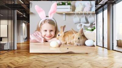 .Easter little girl with rabbit ears holds 2 live rabbits in her hands laughs and looks at the camera in the home kitchen. girl has a video call on paska day Wall mural