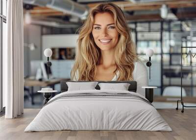 A blonde woman in a white shirt smiles confidently in a modern office setting Wall mural