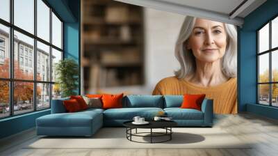 A woman with gray hair sits in a well-decorated living room, exuding warmth and confidence in her casual attire Wall mural