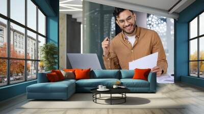 Businessman working on laptop and reviewing documents in modern office Wall mural