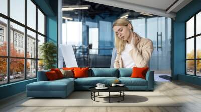 Businesswoman experiencing neck pain while working on laptop in modern office Wall mural