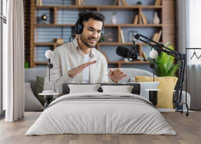 Confident young man recording podcast at home while using laptop and microphone, engaging with audience through live streaming and headphones Wall mural