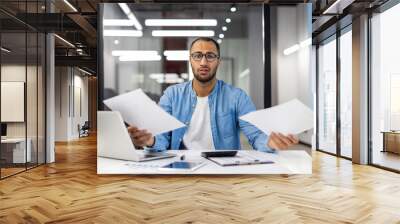 Confused businessman analyzing paperwork in modern office Wall mural