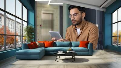 Focused man using a tablet in a modern office environment Wall mural