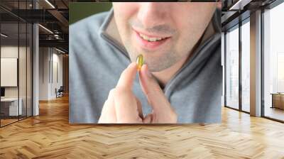 Blurred smiling handsome man in gray sweatshirt on background holding omega 3 soft gel pill in his fingers. Yellow omega 3 vitamin capsules in male hand. Nutritional supplements for people health care Wall mural