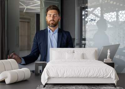 Mature successful senior experienced man meditating in lotus position inside office, businessman with closed eyes resting and visualizing future plans, boss in business suit at workplace Wall mural