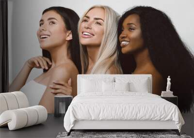 Beauty photo of three smiling multiracial women with different types of skin: Caucasian, African american and Asian girls, isolated over white background. Beautiful  young women with natural make-up. Wall mural