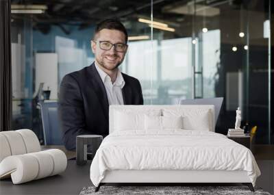 Portrait of a successful male businessman, banker, financial director sitting in the office at the table and using a laptop. Looking and smiling at the camera Wall mural