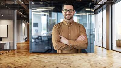 Portrait of a young male programmer, creative designer, developer engineer. He stands in the office with his arms crossed on his chest and looks at the camera with a smile Wall mural