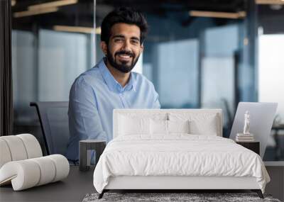 Portrait of happy and successful businessman, indian man smiling and looking at camera, satisfied with achievement results man working inside office building using laptop at work Wall mural