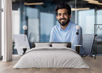 Portrait of happy and successful businessman, indian man smiling and looking at camera, satisfied with achievement results man working inside office building using laptop at work Wall mural