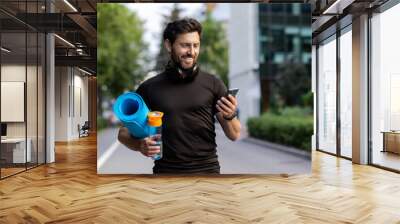 Portrait of mature successful adult athlete, bearded man going to workout, coach holding fitness mat and phone, browsing online app for joint physical training Wall mural