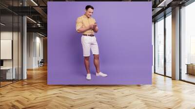 Portrait of positive handsome guy texting chatting cellphone on violet background Wall mural