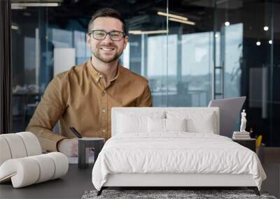 Portrait of young businessman in shirt, man smiling and looking at camera at workplace inside office, accountant with calculator behind paper work signing contracts and financial reports Wall mural