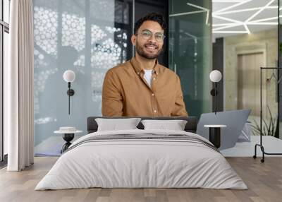 Smiling businessman working on laptop in modern office setting Wall mural