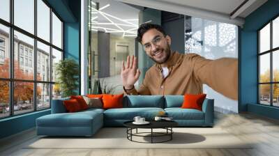 Smiling man waving in modern office during video call Wall mural