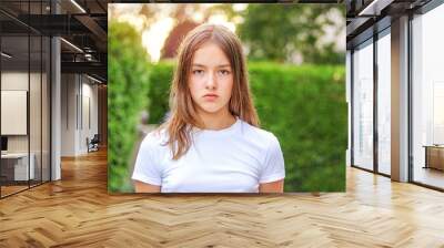 Close-up portrait of serious angry teenager girl outdoors in park with green hedge background. No makeup, natural beauty concept. Summer lifestyle. Facial expression, teenager period Wall mural