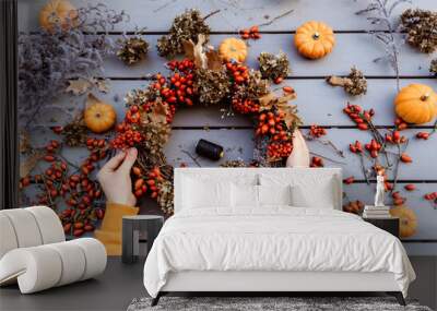 Girl making floral autumn door wreath using colorful rosehip berries, rowan, dry flowers and pumpkins. Fall flower decoration workshop, florist at work. Wall mural