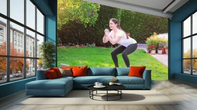 Healthy lifestyle. Exercising at home. Doing fitness online. Beautiful young woman doing sport in garden outdoors following guide of online tutorial or trainer on laptop. Wall mural