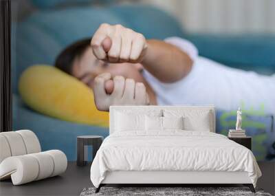 Teenager boy lying on sofa at home showing fig to parents at camera. Teen rudeness and protest. Rude offensive  gestures Wall mural