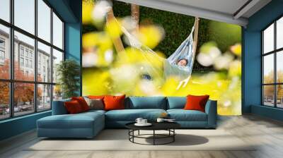 Young girl relaxing having nap in hammock in garden at home at bright sunny day. Slow living, gadget detox and weekend leisure activity. Quarantine and self isolation period Wall mural