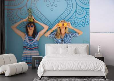 Two young happy women posing with tropical fruits Wall mural