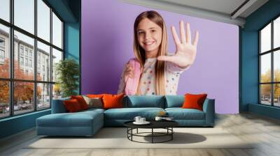 Young cheerful smiling school girl wear backpack showing hello highfive gesture isolated on purple background Wall mural