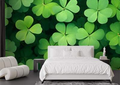 A close-up of a vibrant green four-leaf clover standing tall amidst a blurred green background. The leaves are glossy and well-defined, capturing the sunlight beautifully. Wall mural