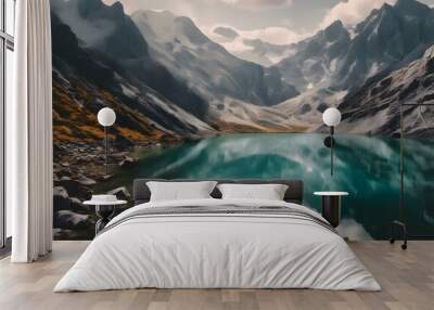 A serene mountain lake surrounded by autumn trees and snow-capped peaks, reflecting the landscape in its calm waters under a partly cloudy sky. Wall mural