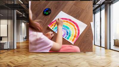 Kids at home. A child girl paints a rainbow on paper indoor during the quarantine for the coronavirus pandemic. Social campaign in support of society. let's all be well. Stay home Wall mural