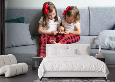 Two little girls sitting on sofa and playing on smartphone. sisters have fun with a mobile phone, watch a children's movie or cartoon. Technology of the new generation are addicted to gadgets concept  Wall mural