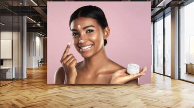 Skincare, face and woman with cream container in studio isolated on a pink background. Product, dermatology creme and portrait of happy Indian female model apply lotion, moisturizer and cosmetics. Wall mural