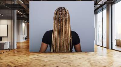 Brunette woman with braids in her hair, wearing jeans and a black blouse, sitting on the studio floor with her back to the camera. Wall mural