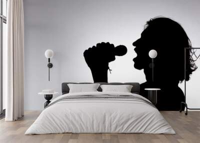 Silhouette of young man holding wireless microphone singing music with emotion. Wall mural