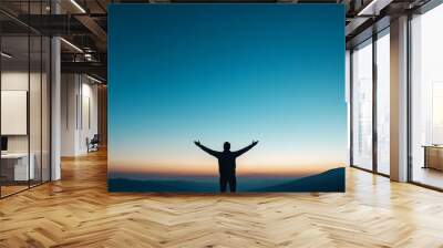 A silhouette of a person with arms raised against a stunning twilight sky. Symbolizes freedom, joy, and connection with nature. Wall mural