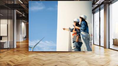 two engineers are  wearing hard hats and orange vests are pointing at a wind turbine. They are looking at the turbine and possibly discussing its design or operation Wall mural