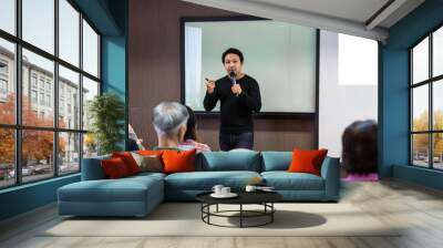 Asian Speaker or lecture with casual suit on the stage in front of the room presenting with the screen in the conference hall or seminar meeting room, business and education concept Wall mural