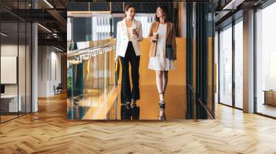 Two asian businesswomen walking and talking during coffee break in modern office or coworking space, coffee break, relaxing and talking after working time, business and people partnership concept Wall mural