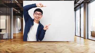 Young man wearing glasses gesture point finger at copy space portrait white background Wall mural