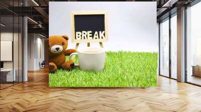 Bear is sitting down with a cup of coffee on green grass Wall mural