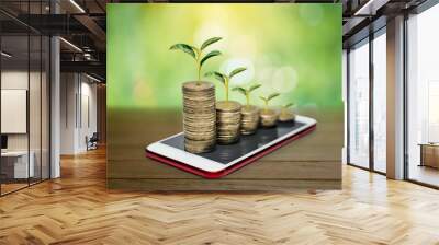 Business and financial metaphor of plants growing on stack money coins with blurred green nature background and copy space Wall mural