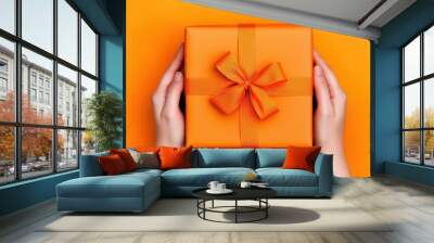 Hands securely tying a bow around an orange gift box on a vibrant background celebrating the art of present wrapping Wall mural