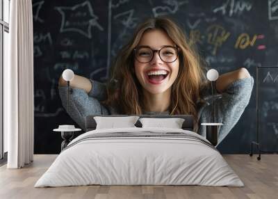 A cheerful woman in glasses poses in front of a blackboard with chalk writing, exuding charm and enthusiasm Wall mural