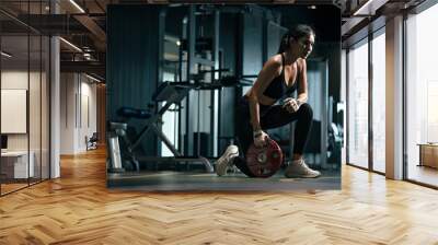 Young asian woman exercising with weight plate in the gym. Wall mural