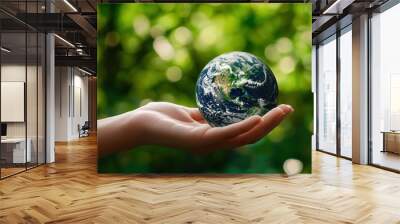 A hand holds a miniature Earth globe, symbolizing care for the planet amidst a vibrant green background. Wall mural