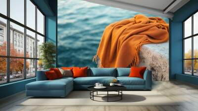 An elegant orange blanket draped over a textured stone ledge by the tranquil sea, perfect for cozy moments or stylish decor. Wall mural