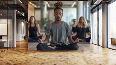 A group of people are sitting in a room and meditating. The man in the center is wearing a gray shirt and has tattoos on his arm Wall mural