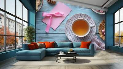 A pink card with a ribbon is on a table next to a cup of tea Wall mural